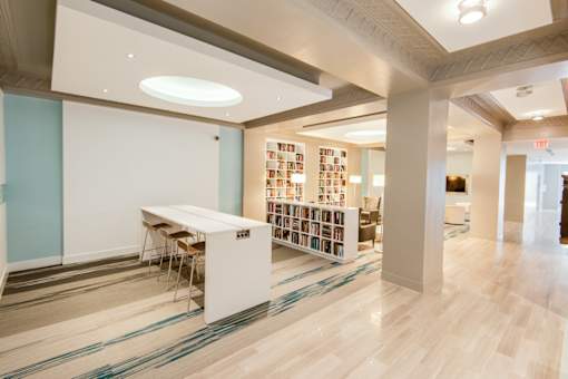 A room with a long table and chairs with a bookshelf in the background.