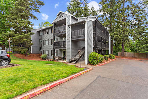 A grey apartment building with a car parked in front.