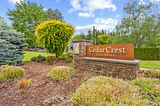 A sign for Cedar Crest Apartments is surrounded by shrubbery and trees.