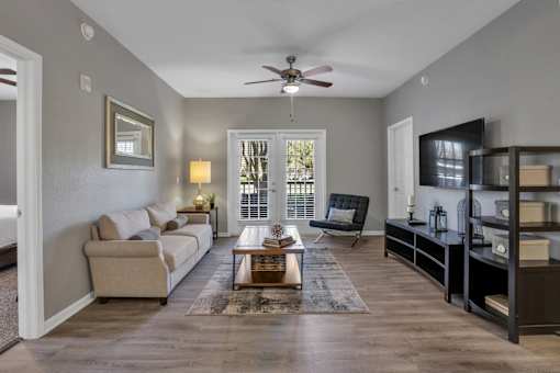 A living room with a beige couch, a coffee table, and a ceiling fan.