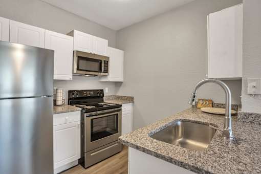 A kitchen with a stainless steel refrigerator, microwave, oven, and sink.