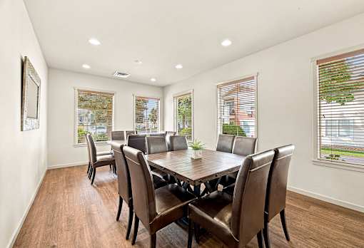 A large brown dining table with chairs is in a room with windows.