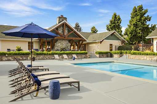 A pool with sun loungers and a blue umbrella in front of a house.