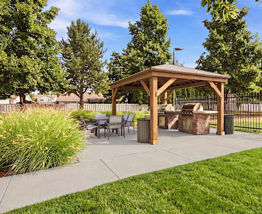 A wooden gazebo is surrounded by trees and a fence.