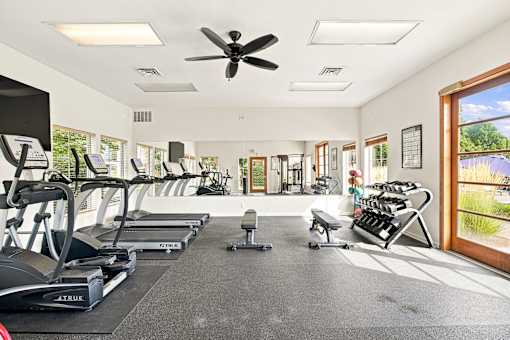A spacious gym with treadmills, elliptical machines, and a fan.