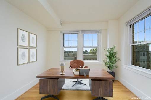 A virtual staged image of a room with a desk, chair, and pictures on the wall.