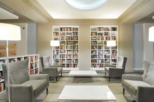 A living room with grey couches, a white rug, and a bookshelf filled with books.