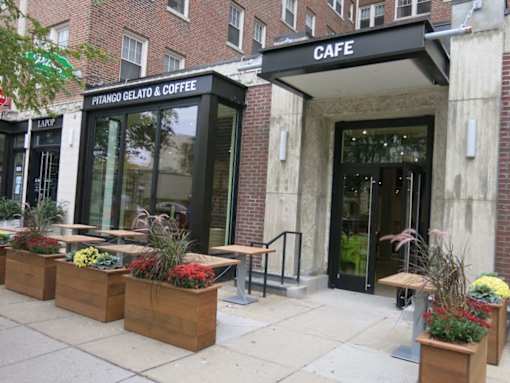 A cafe with a black awning and wooden planters in front.