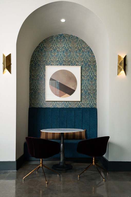 A blue and gold patterned wall with a round mirror and two chairs.