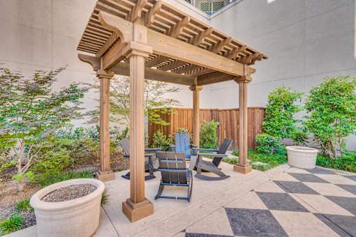 A wooden pergola with a checkered floor and chairs underneath.