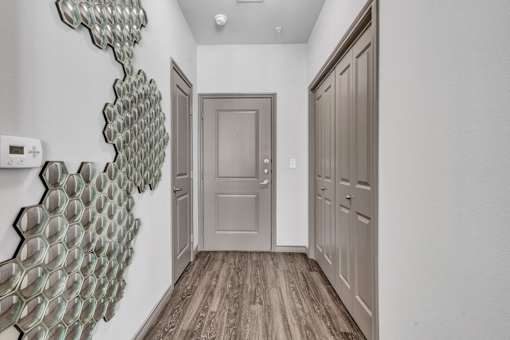 A hallway with a large art piece on the wall and wood flooring.