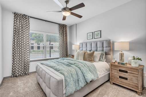 A bedroom with a bed, nightstand, and window with curtains.