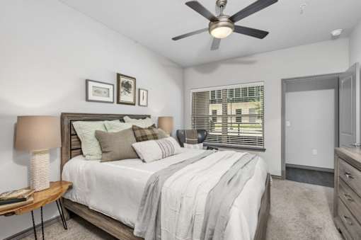 A bedroom with a bed, a ceiling fan, and a window with blinds.