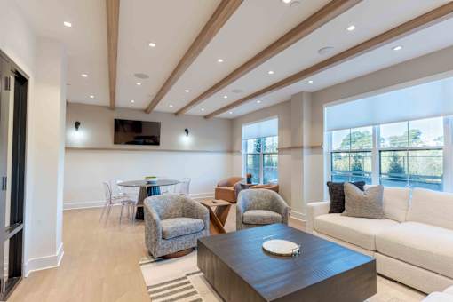 A modern living room with Community lounge with cozy seating, exposed wood ceiling beams, and bright window views at Creekline at Fairfield apartments, Fairfield CT. 