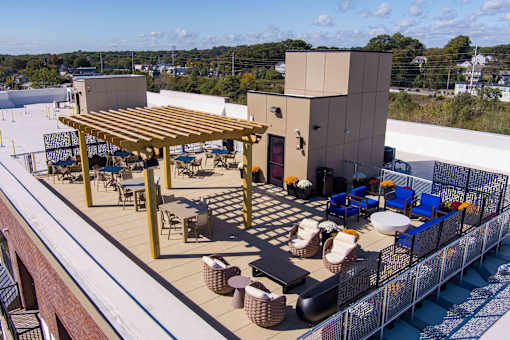 Aerial view of the rooftop terrace at Creekline at Fairfield apartments in Fairfield, CT featuring a pergola, outdoor dining tables, lounge seating, and resident gathering areas.