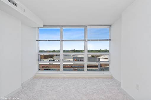 A large empty room with a view of a parking lot through the windows.