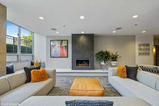 A modern living room with a grey couch, a yellow ottoman, and a fireplace.