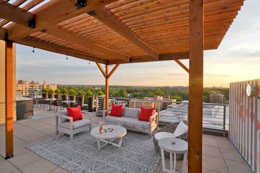 A wooden patio with a table and chairs overlooking a cityscape at sunset.