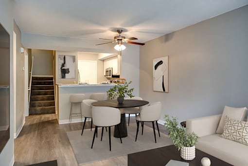 A living room with a white couch, a round table with chairs, and a ceiling fan.
