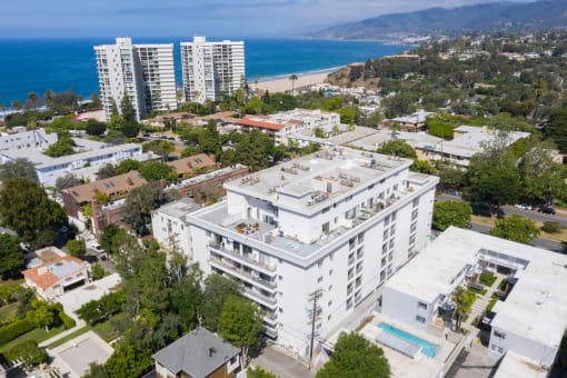 Apartments for Rent in Santa Monica, CA - San Vicente Tower - Aerial View of Property Exterior with White Walls, Surrounding Lush Green Neighborhood, Showcasing the Units and the Pool, with the Nearby Beach in View