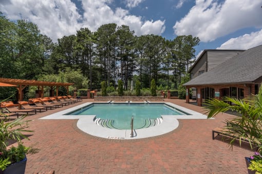 Pet-Friendly Apartments in Lawrenceville– Park on Sweetwater – a pool with chairs and a house with trees in the background