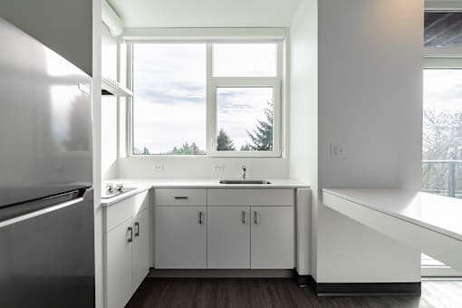 A kitchen with white cabinets and a window overlooking the trees.