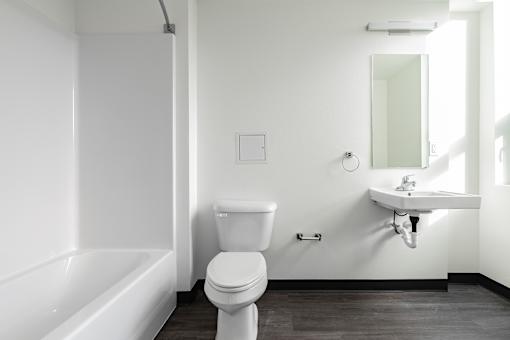 A white toilet sits in a bathroom next to a bathtub.