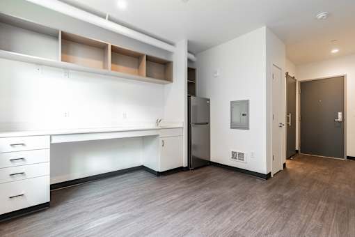 A white desk with drawers and a white cabinet with shelves are in a room with a wood floor and a white wall.
