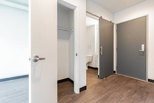 A white door with a silver handle is open to a hallway with a brown door on the right.