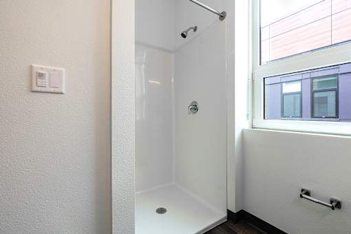 A white bathroom with a glass shower door and a window.