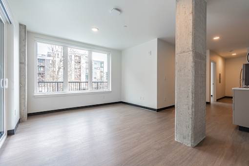 A large empty room with a concrete pillar and wooden flooring.