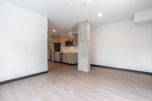 A room with a column in the middle and a kitchen area in the background.