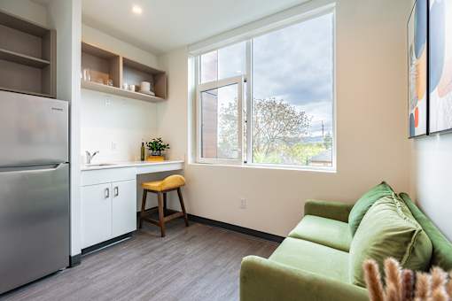 A kitchen with a refrigerator, a bar stool, and a couch.