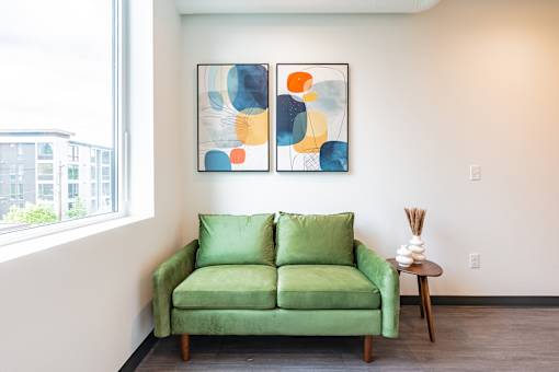 A green couch sits in front of a window with a painting on the wall.