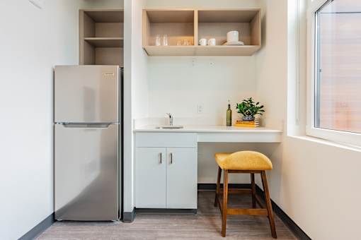 A small kitchen with a refrigerator, a sink, and a stool.