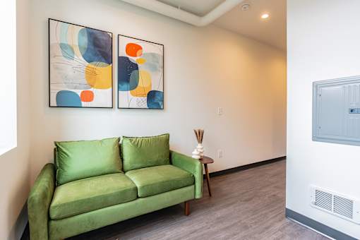 A green couch sits in a room with two framed artworks on the wall.