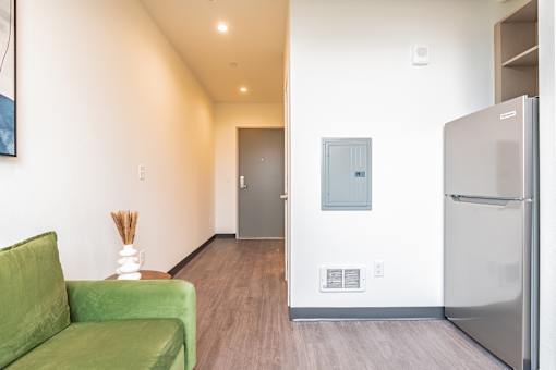 A green couch sits in a hallway with a refrigerator on the right.