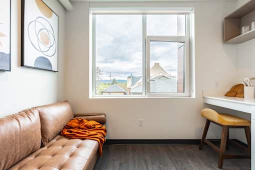 A brown leather couch with an orange throw blanket sits in front of a window.