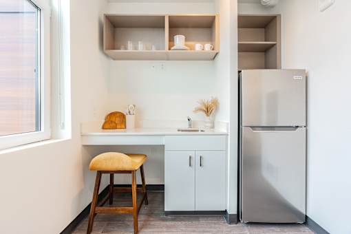A kitchen with a stool, a fridge and a counter.