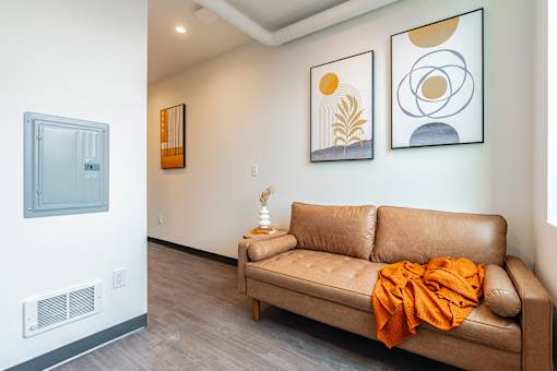A tan couch with an orange throw sits in a room with two framed pictures on the wall.