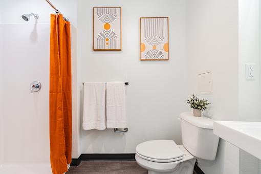 A bathroom with a toilet, sink, and orange shower curtain.