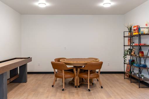 A room with a pool table, a table and chairs, and a shelf with various items.