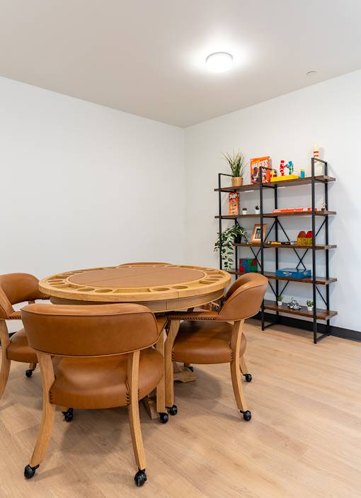 A round wooden table surrounded by chairs in a room with a shelf in the background.