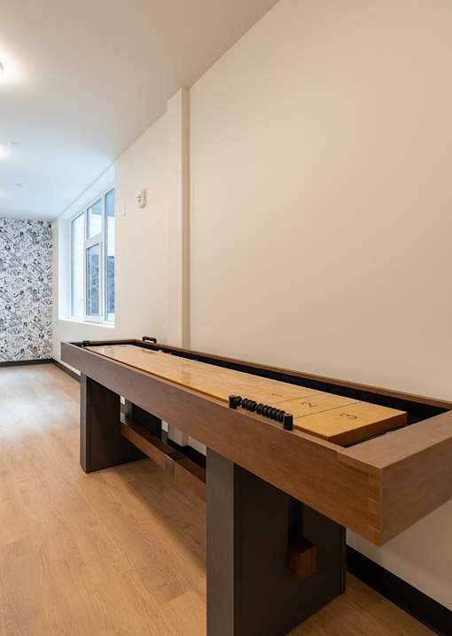 A pool table with a brown cloth and white balls is in the middle of a room with a window and curtains.