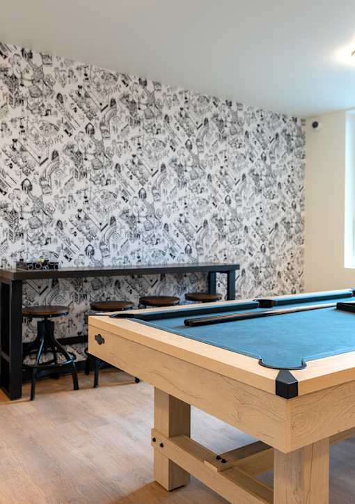 A pool table with a blue cloth and a wallpapered wall.