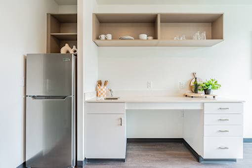 A kitchen with a refrigerator, white desk, and drawers.