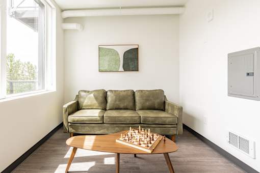 A room with a green couch, a wooden coffee table with a chess board on it, and a painting on the wall.