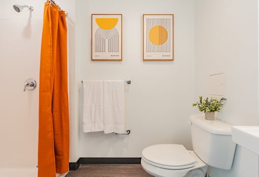 A bathroom with a toilet, sink, and orange shower curtain.
