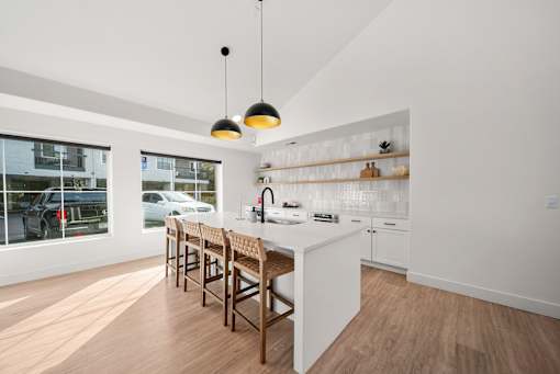 A modern kitchen with a white counter and wooden chairs.