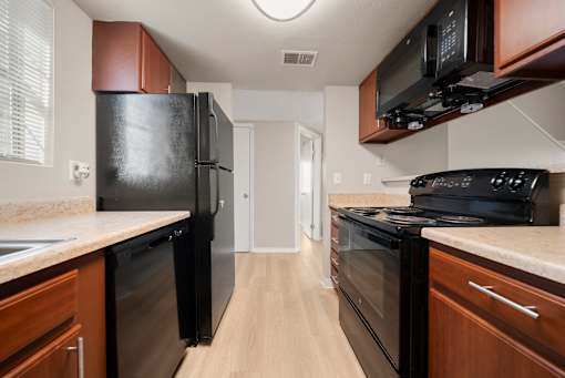 Aurora, CO, Apartments Near Coors Field - The Juliet at Lowry - Kitchen with Plank Flooring, Wood Cabinetry, and Black Appliances.